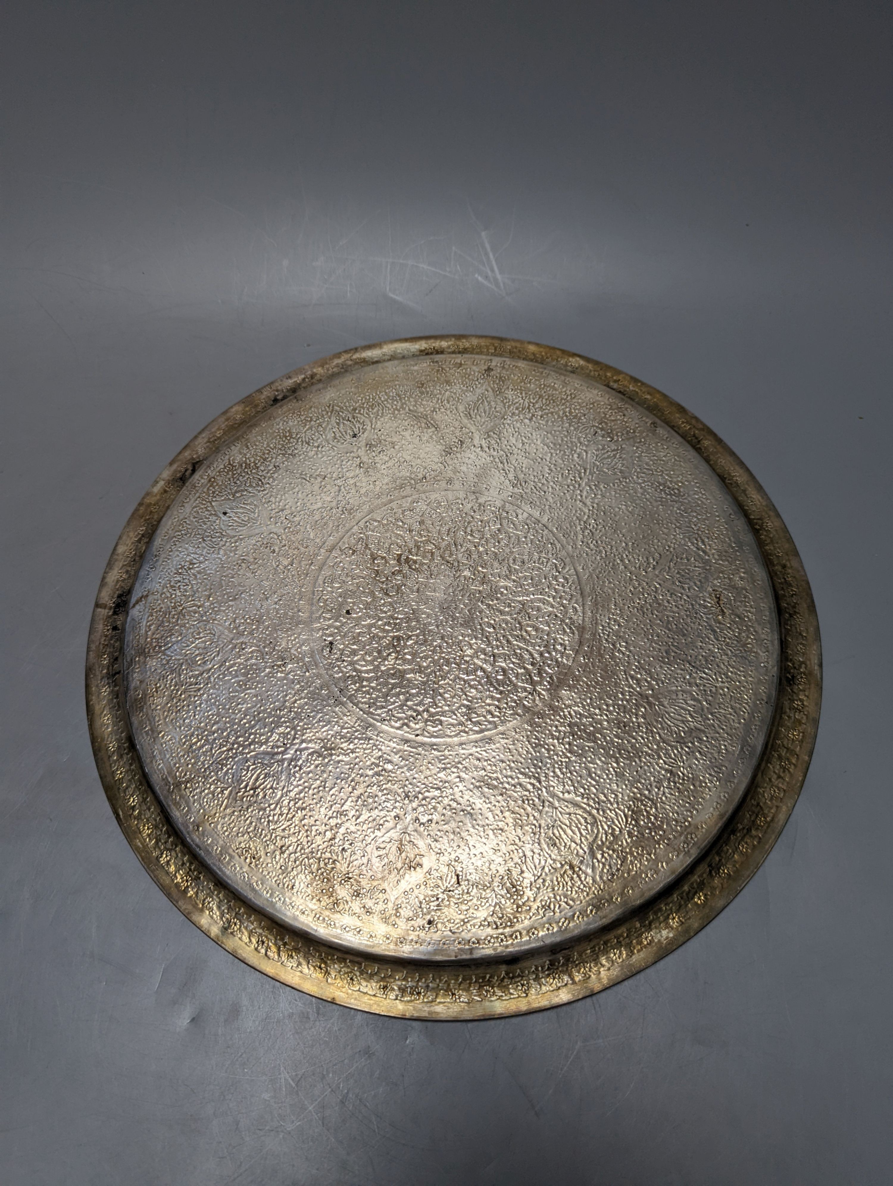A Persian engraved white metal circular drink's tray by Vartan, 32cm, 747 grams and a white metal wall plaque.